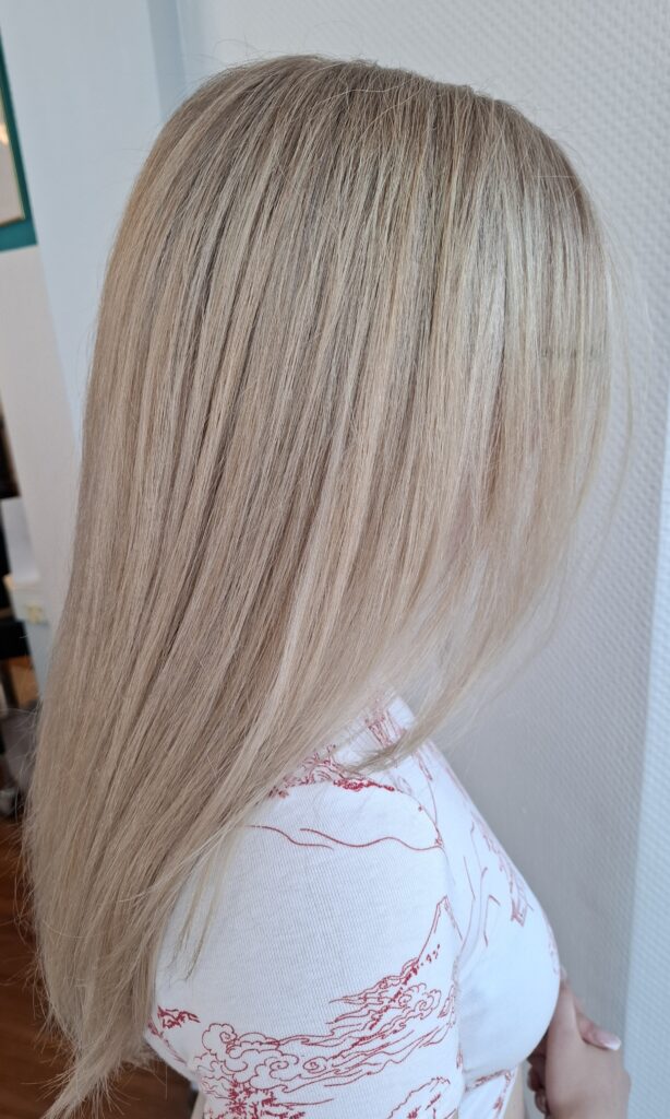 Back view of a person with long, straight platinum blonde hair, wearing a white top.